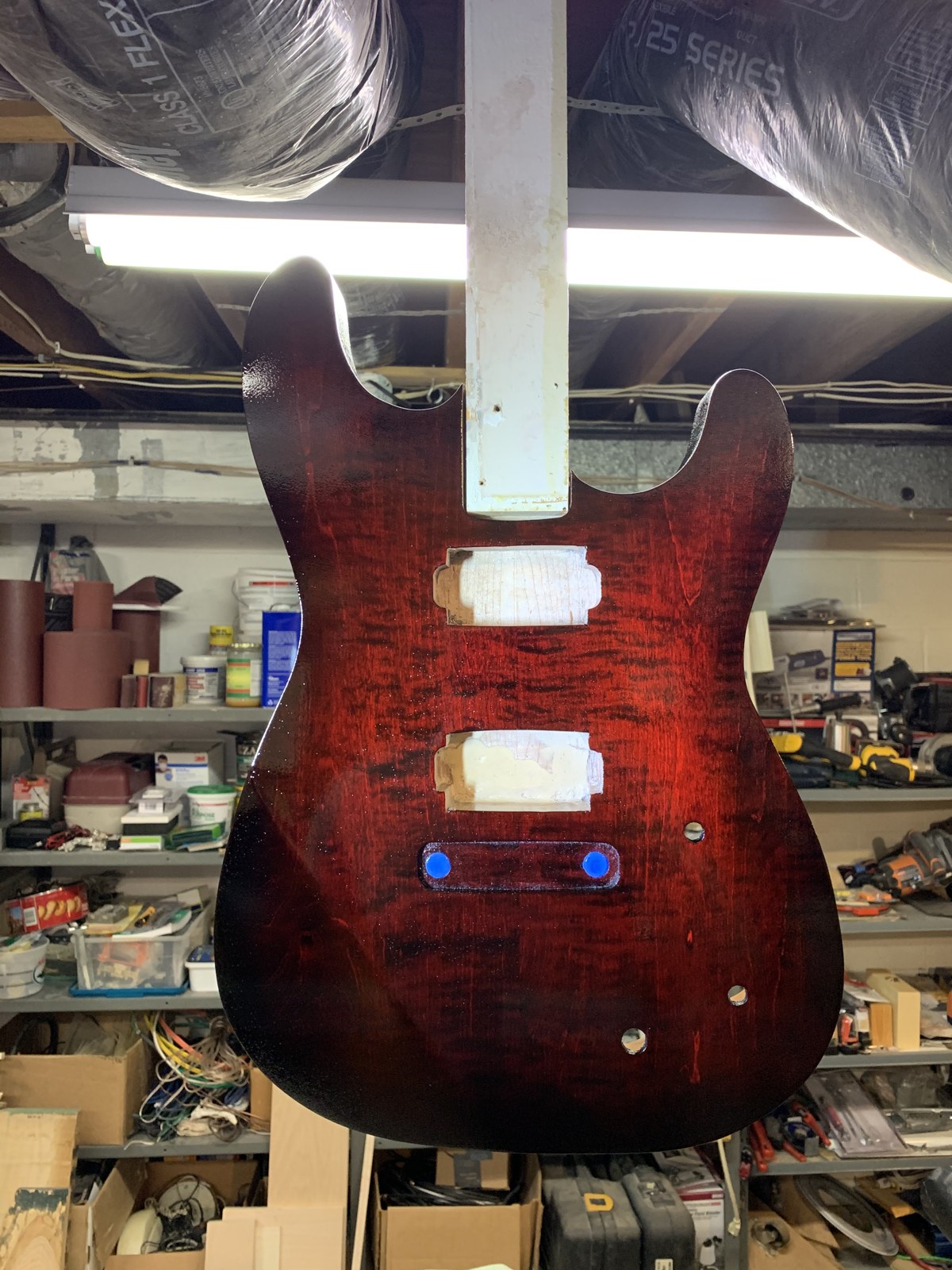 Red stained guitar body hanging with its cavities masked
