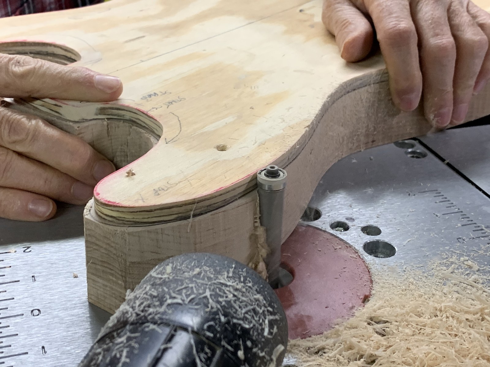 Bare guitar body being shaped at a spindle sander