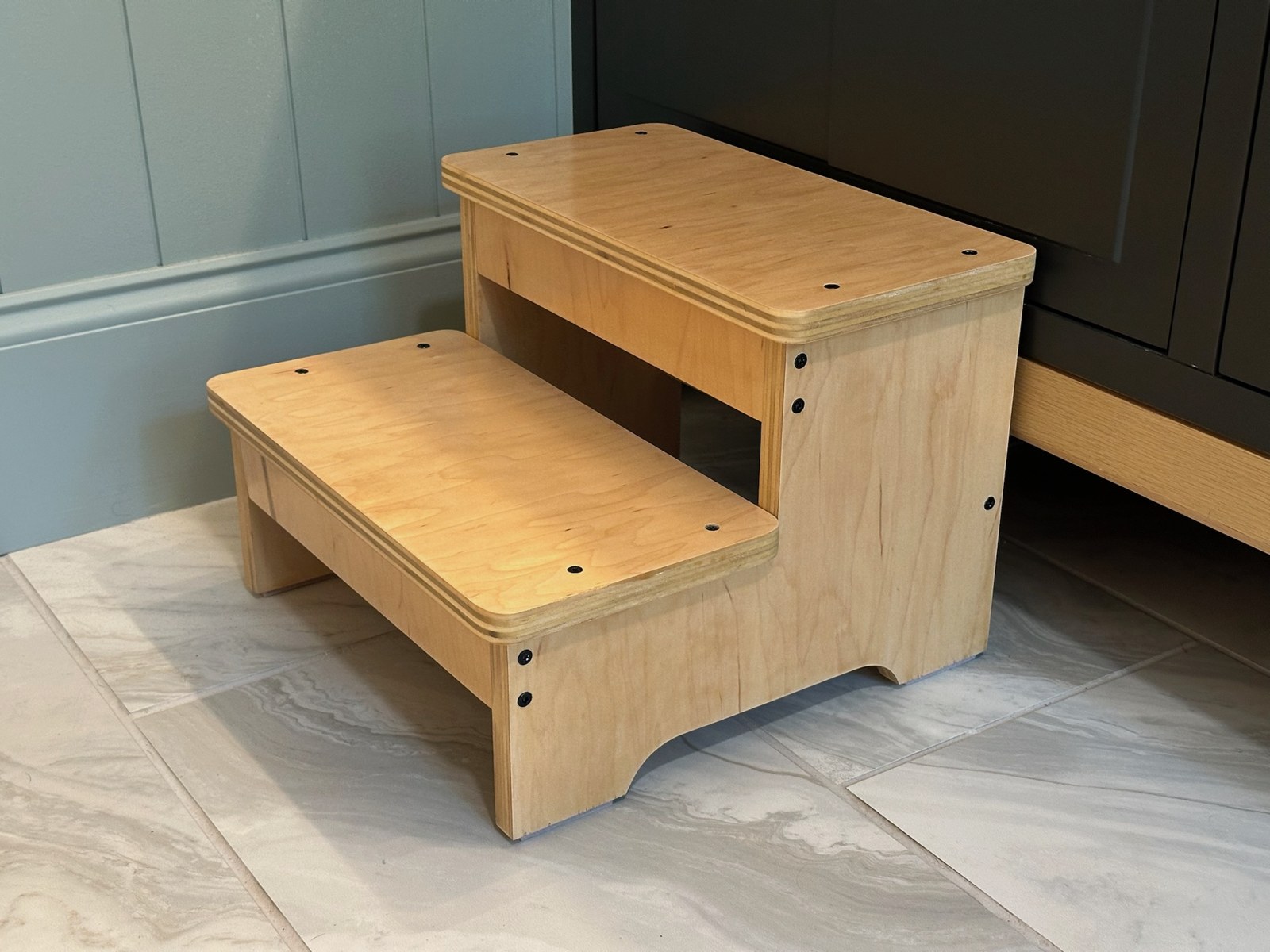 Completed two-step wooden stool with rounded corners beside a cabinet